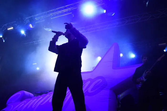 Silhouette des Sängers Sampagne, der unter blauem Bühnenlicht in ein Mikrofon singt, vor einem großen Stern-Element.
