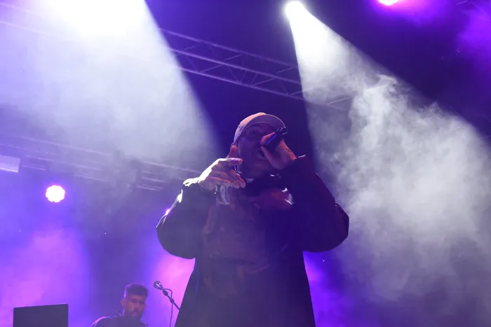 Azad performt unter violetten Scheinwerfern und Nebel auf einer Bühne mit einem Mikrofon in der Hand.