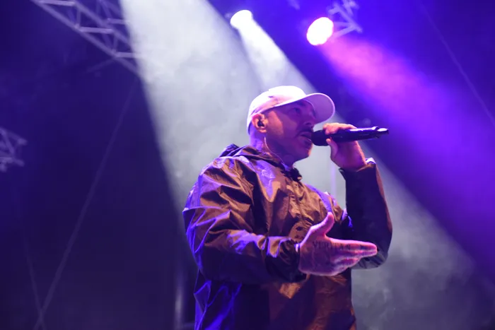 Azad singt mit weißer Kappe und dunkler Jacke unter lila und weißem Bühnenlicht in ein Mikrofon.