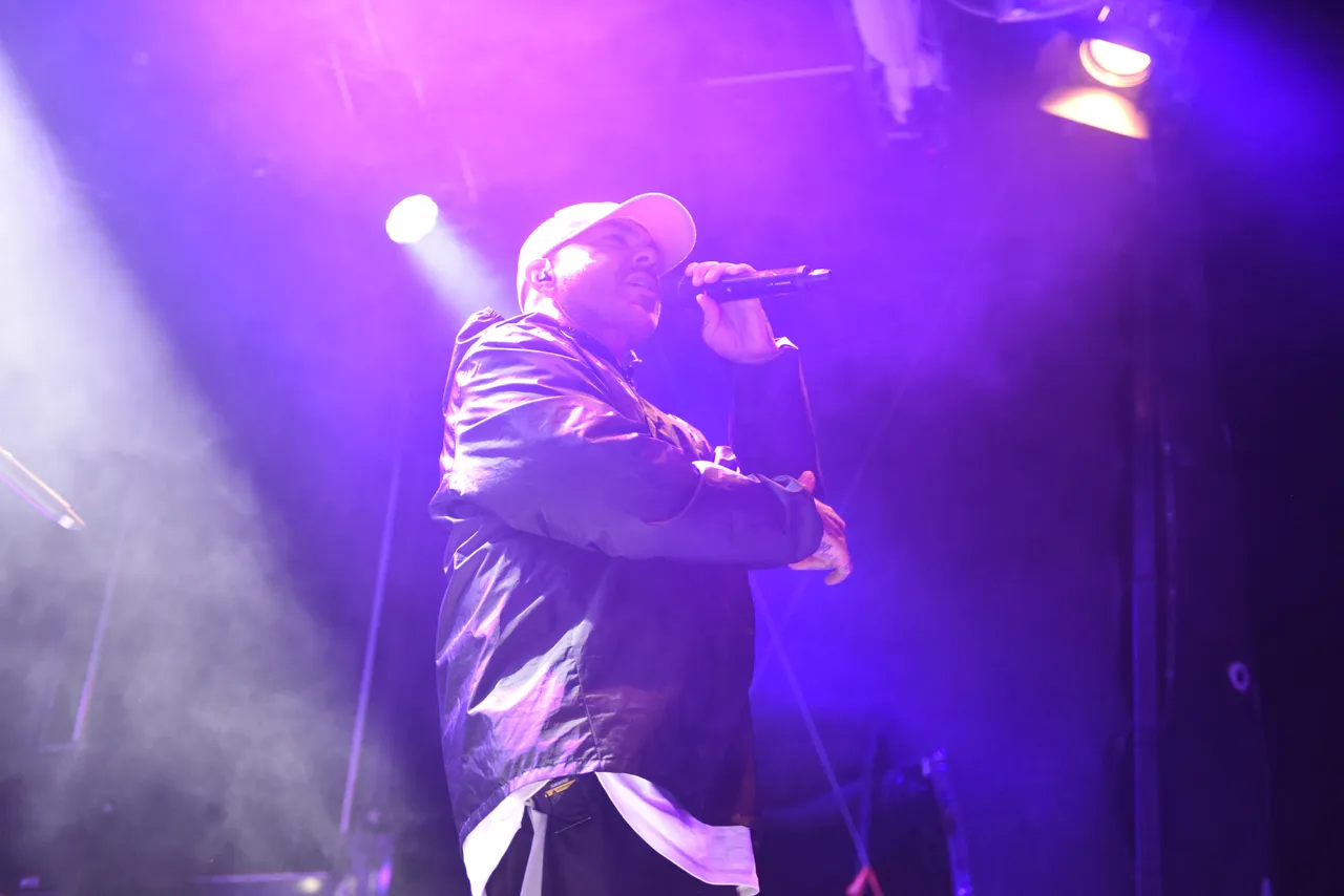 Azad performt unter violettem Bühnenlicht mit einem Mikrofon.