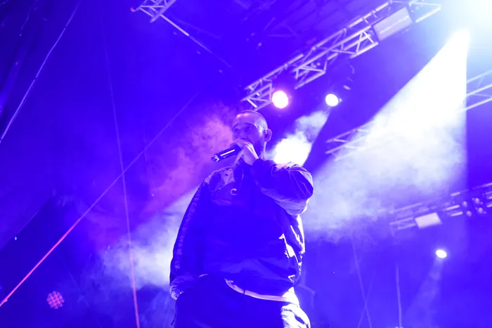 Der Rapper Azad performt mit einem Mikrofon auf einer Bühne unter blauem und violettem Licht.
