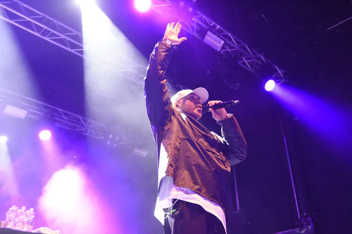 Der Rapper Azad performt mit erhobener Hand und Mikrofon auf einer Bühne unter violettem Licht.