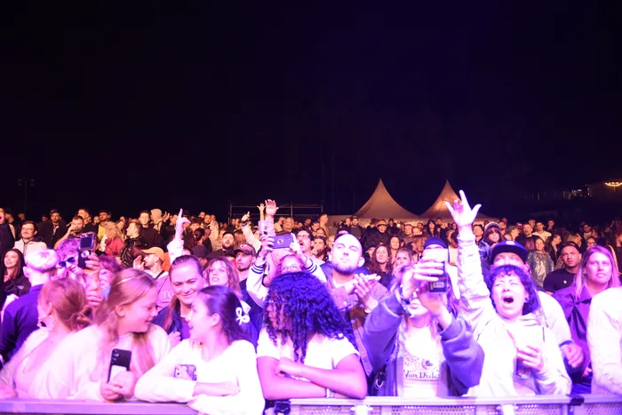 Eine Menschenmenge bei einem Konzert unter violettem Licht hält Smartphones hoch.