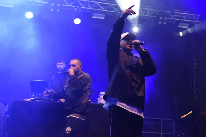 Azad performt mit einem Mikrofon auf einer Bühne unter blauem Licht und Nebel, während im Hintergrund ein weiterer Mann zu sehen ist.