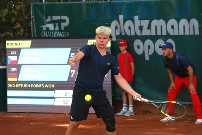 Diego Dedura schlägt einen Tennisball auf einem Sandplatz vor einer Anzeigetafel.