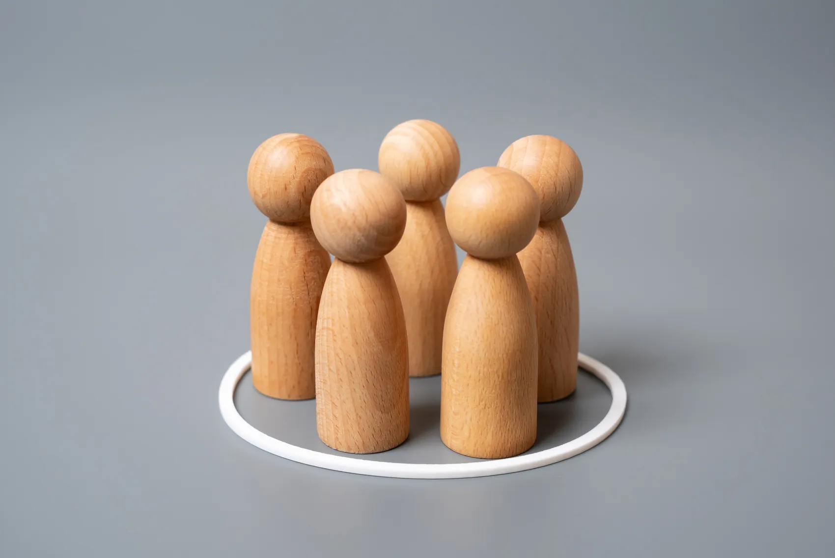 Fünf hölzerne Figuren stehen eng beieinander in einem weißen Kreis auf grauem Hintergrund.
