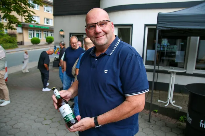 Thomas Schäfer lächelt und hält eine Flasche Bier der Marke Iseri in den Händen.