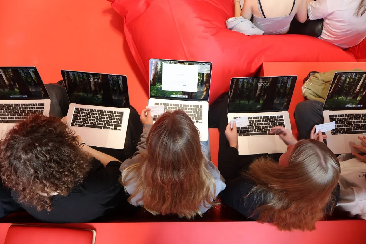 Fünf Jugendliche arbeiten an Laptops und halten Karten, während sie am Planspiel „Start Up Lab“ im Tumo Lüdenscheid teilnehmen.