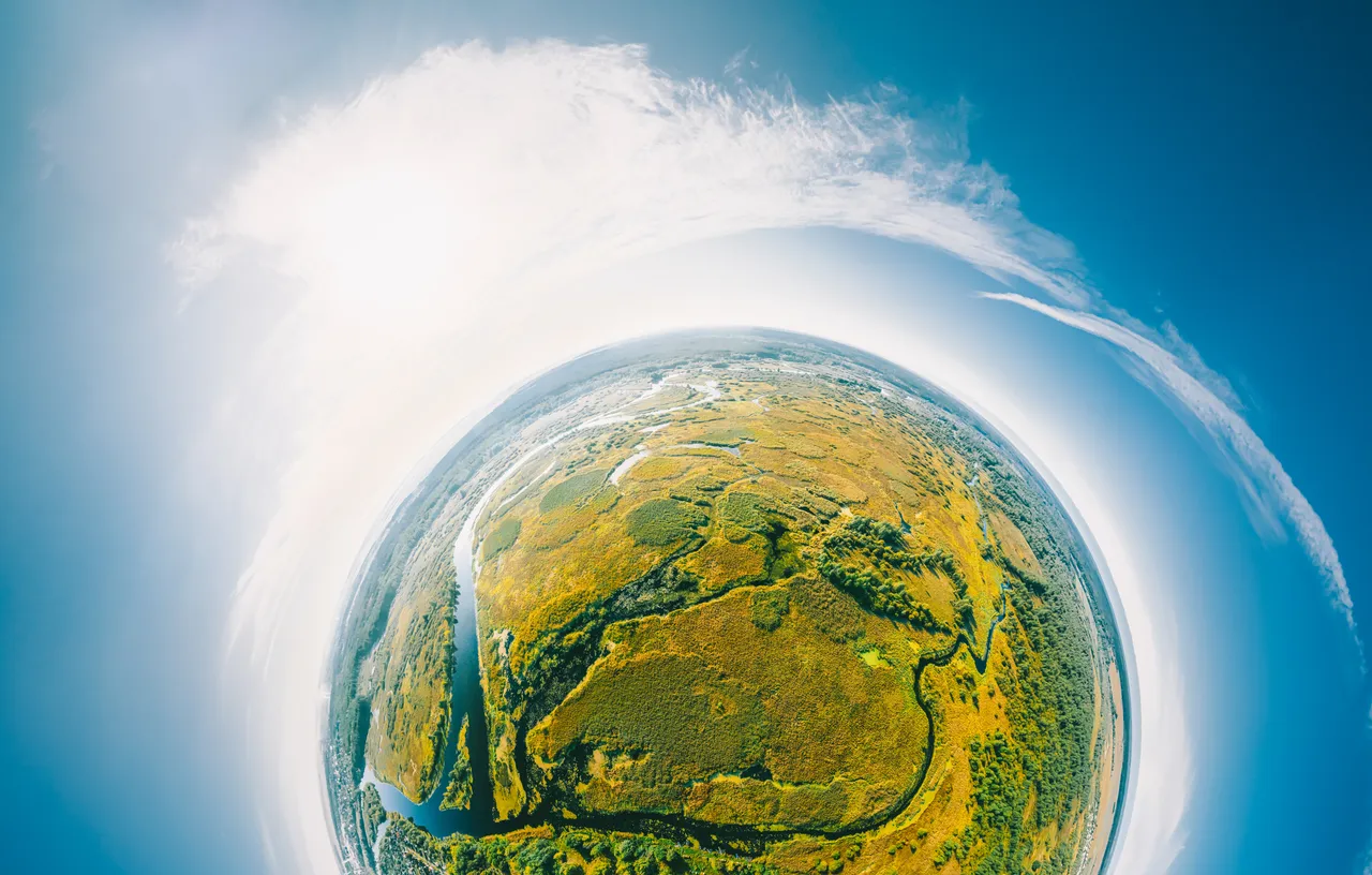 Luftaufnahme einer Flusslandschaft mit grünen und gelben Wiesen unter einem hellen, blauen Himmel in Fisheye-Perspektive.