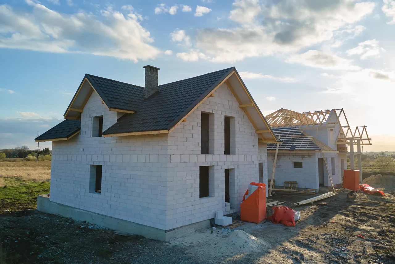 Rohbau eines Hauses mit hellen Ziegeln und dunklem Dach, daneben ein Gerüst für einen Anbau.