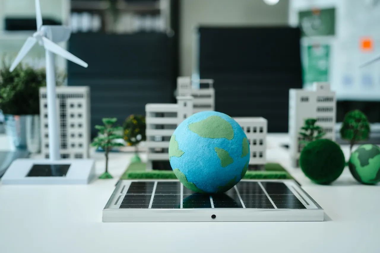 Miniaturmodell einer nachhaltigen Stadt mit einer Erdkugel auf einem Solarpanel, einer Windkraftanlage und kleinen Gebäuden.