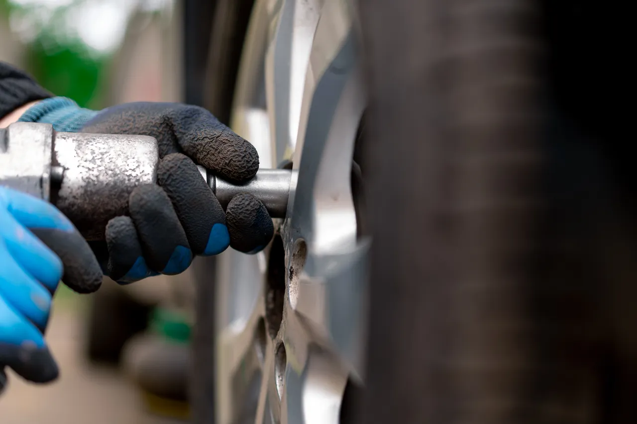 Eine Hand mit Handschuhen löst Radmuttern an einem Autoreifen mit einem Schraubenschlüssel.