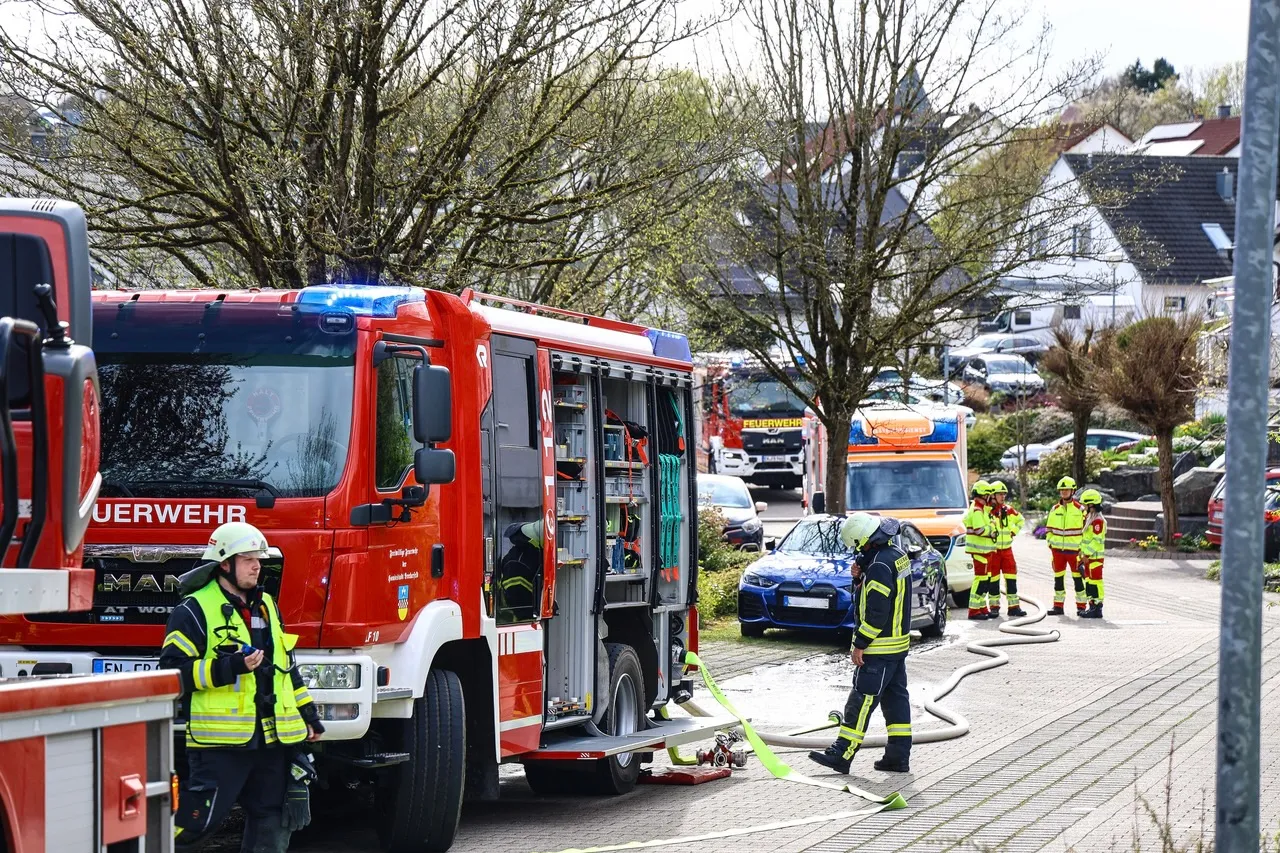 Mehrere Feuerwehrfahrzeuge und Einsatzkräfte an einem Einsatzort. Im Vordergrund ein roter Feuerwehrauto mit geöffneter Heckklappe, aus der ein weiteres Fahrzeug geborgen wird.