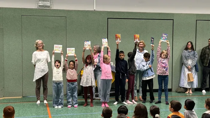 Eine Gruppe von Kindern und Erwachsenen steht in einer Reihe und hält gemeinsam verschiedene Bücher hoch.