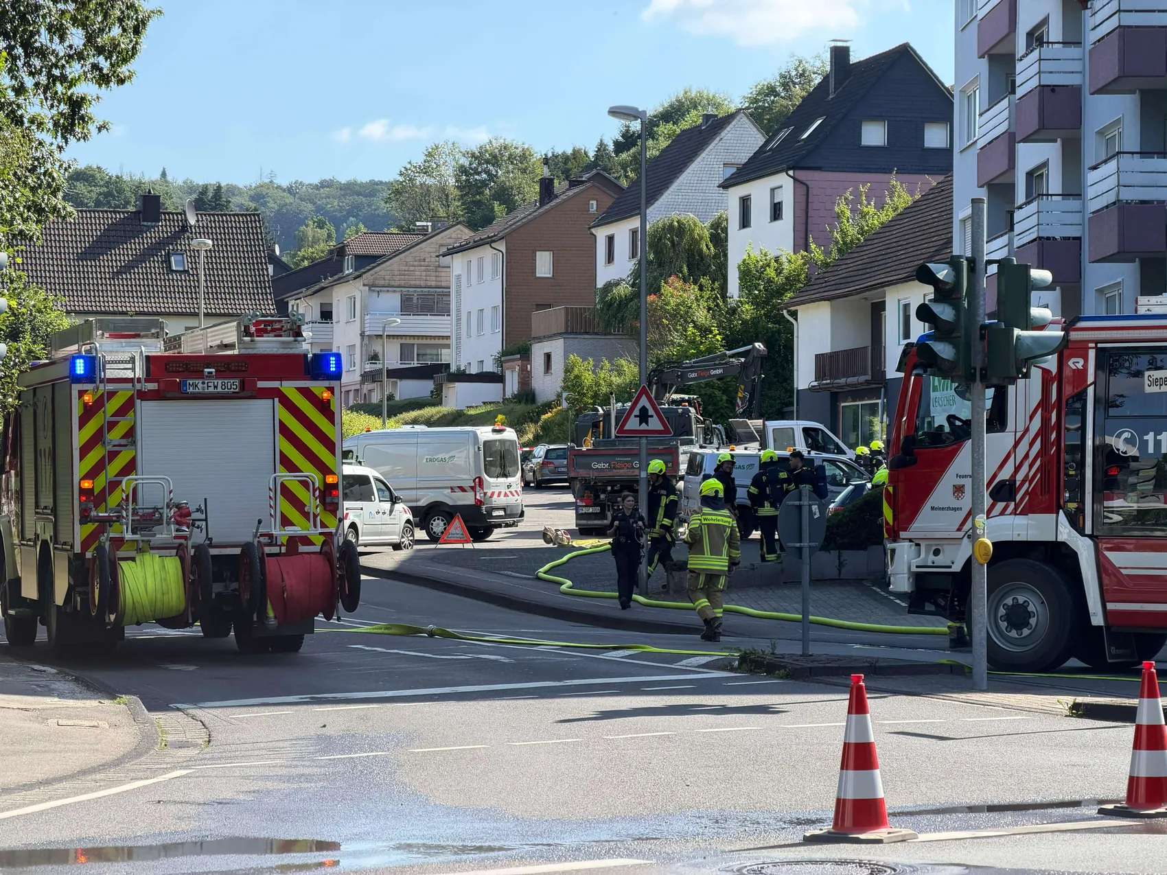 Feuerwehrleute sichern eine beschädigte Gasleitung an einer Kreuzung in Meinerzhagen, während mehrere Einsatzfahrzeuge die Straße blockieren.