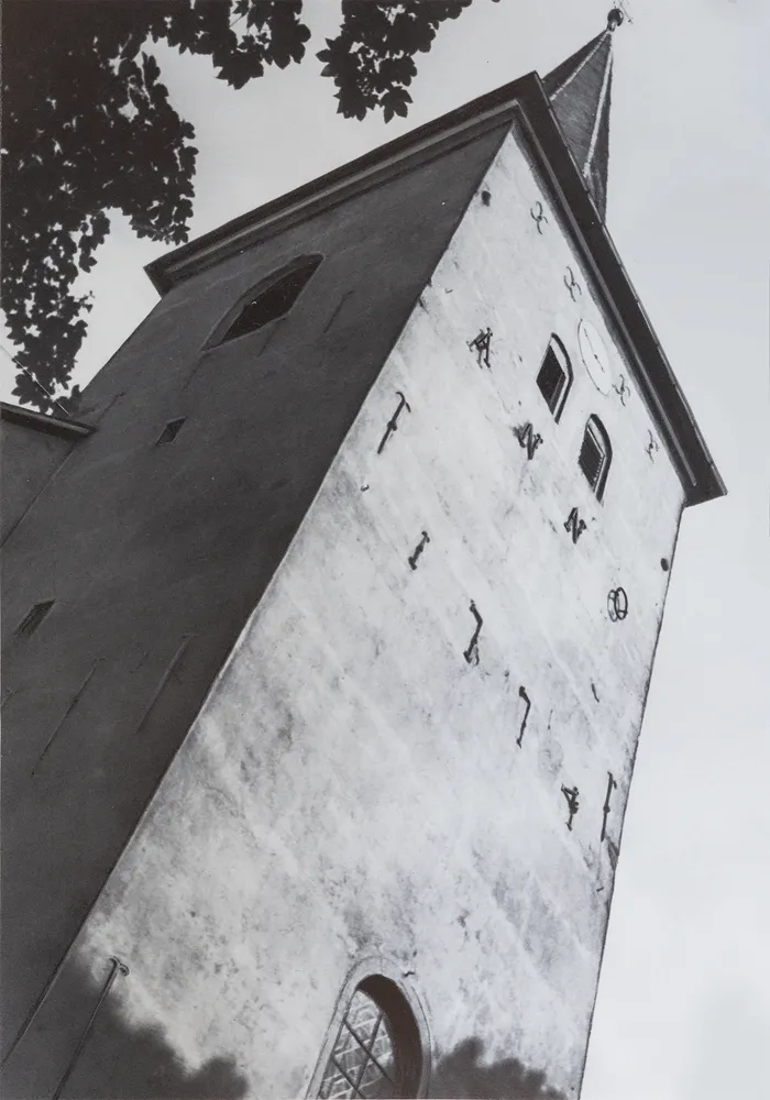 Der Kirchturm der Nicolai-Kirche ist aus einem niedrigen Winkel fotografiert und zeigt die Fassade mit einigen Fenstern und Verzierungen. Der Himmel ist hell und bildet einen Kontrast zum dunklen Turm.