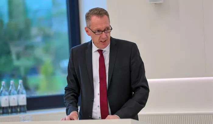 Kai Elsweier mit Brille, dunklem Anzug und roter Krawatte spricht hinter einem Pult.
