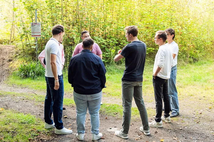 Eine Gruppe junger Männer steht im Gespräch in einem Kreis in einer bewaldeten Umgebung.