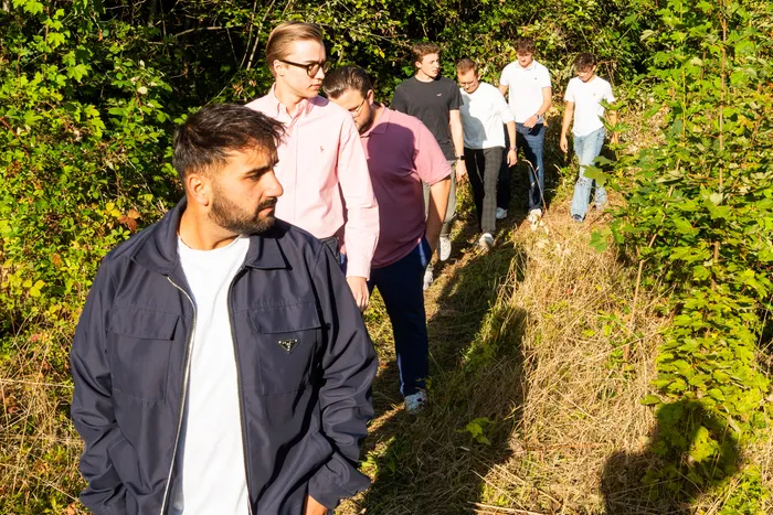 Eine Gruppe junger Männer geht hintereinander auf einem Pfad durch dichtes Gebüsch.