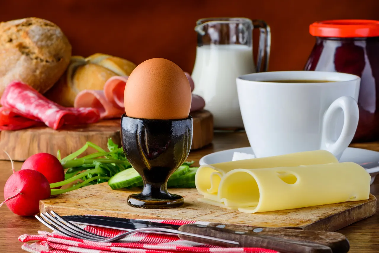 Ein Frühstück mit einem Ei im Eierbecher, Käsescheiben, Radieschen, Brot, Kaffee und Milch.