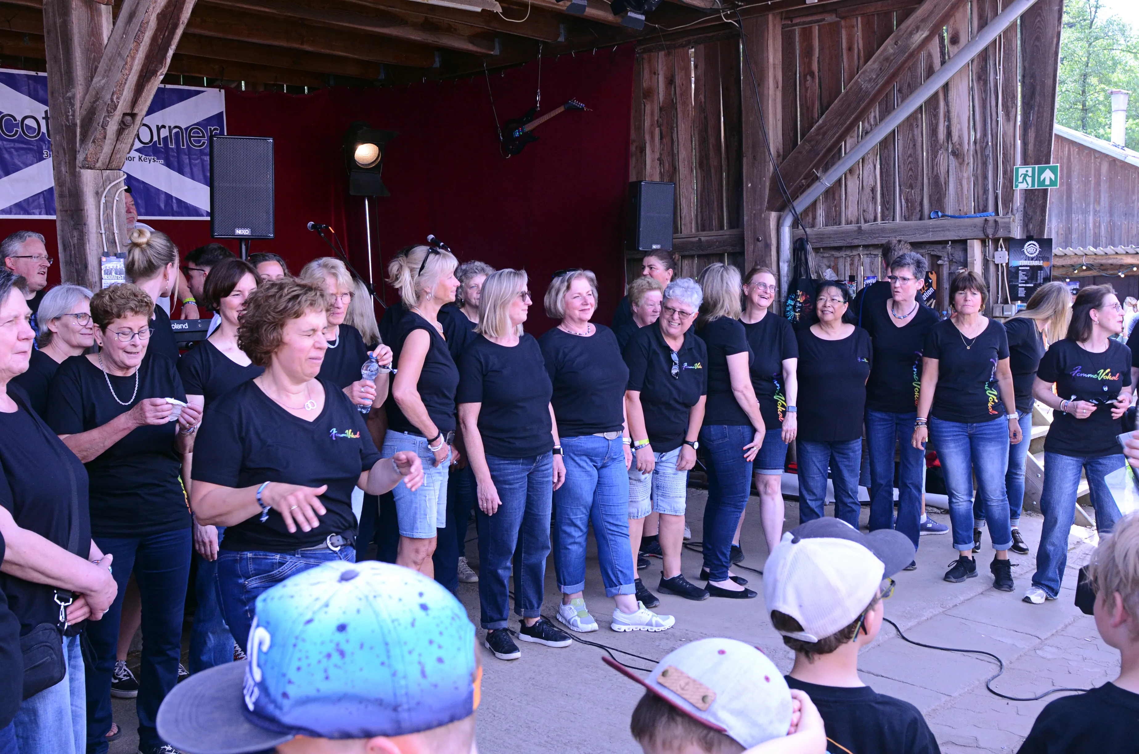 Große Gruppe von Frauen in schwarzen T-Shirts und Jeans steht auf einer Bühne und singt oder tanzt beim I-Rock Festival in Plettenberg.