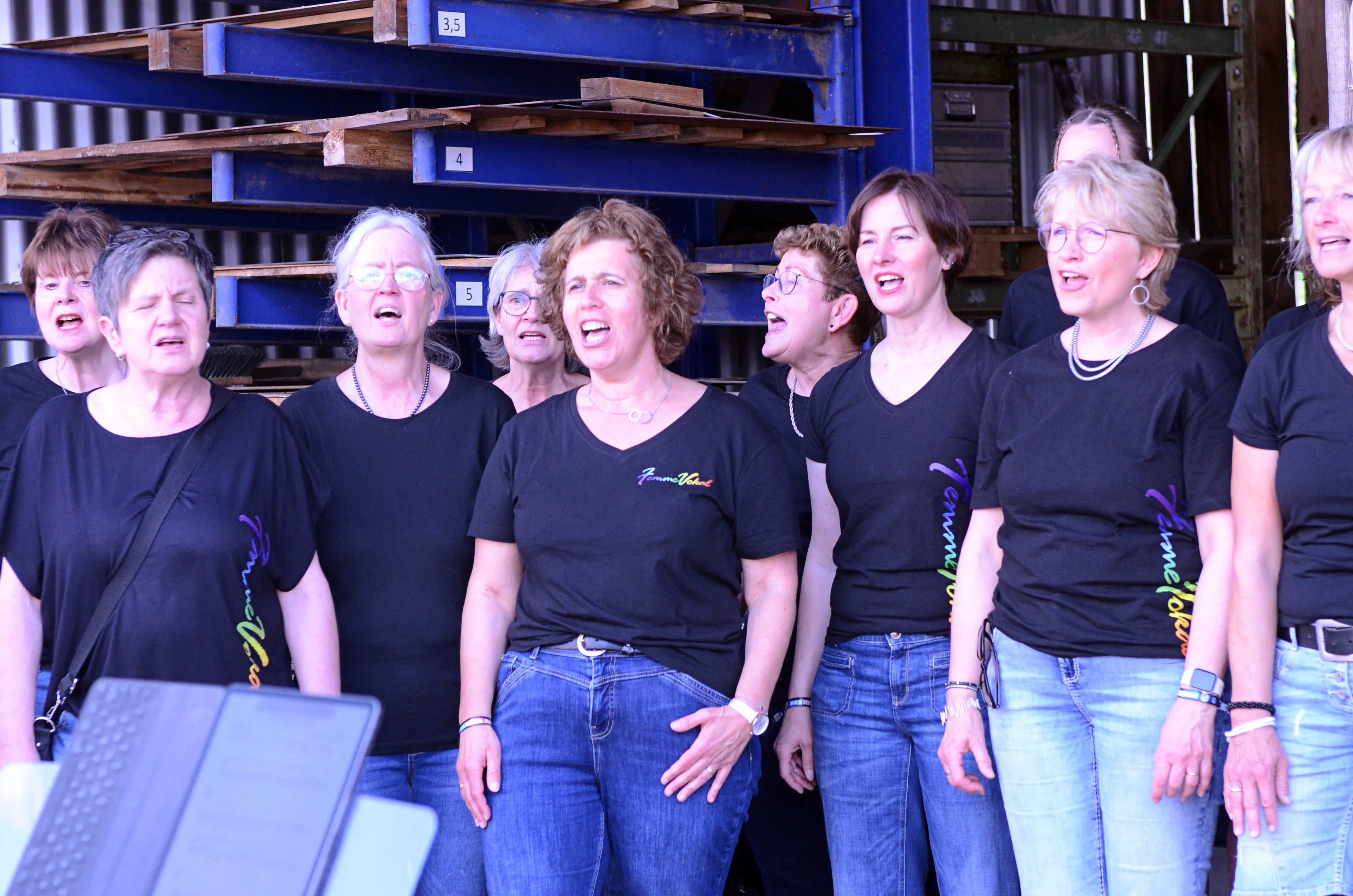 Chor „Femmevokal“ singt auf der Bühne des Immecke Rock Festivals in Plettenberg. Die Sängerinnen tragen schwarze T-Shirts und zeigen beim Singen offene Münder.