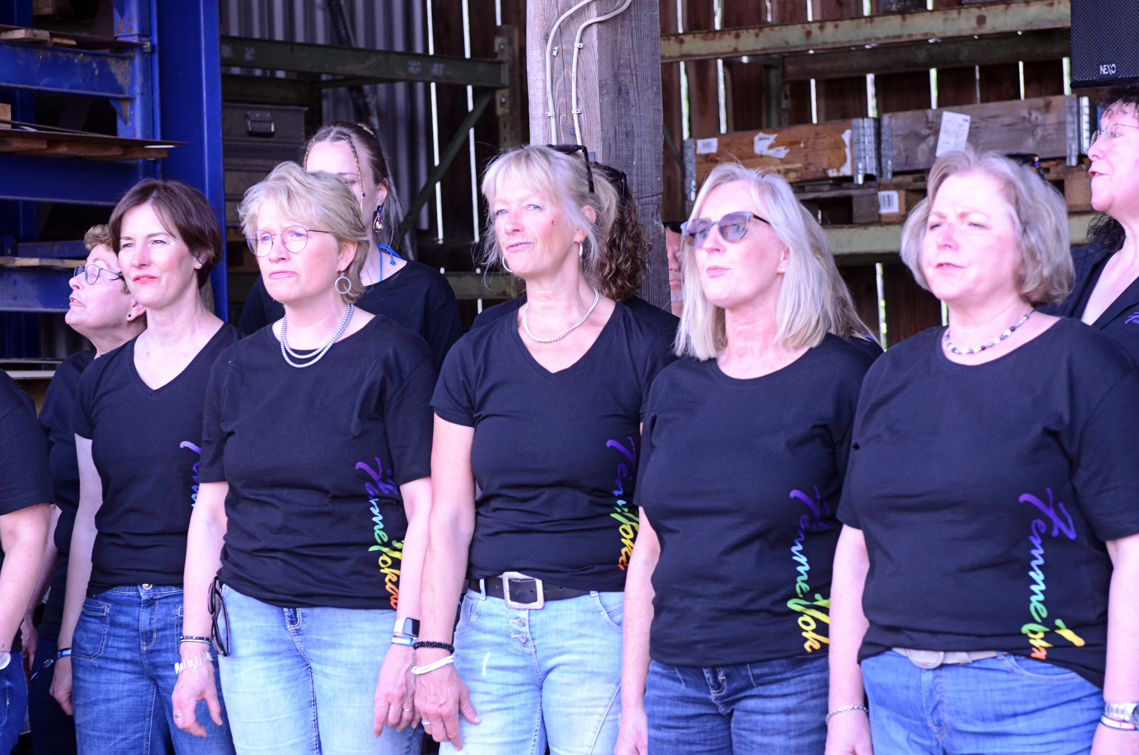 Sechs Frauen stehen eng nebeneinander und blicken nach vorne. Sie tragen schwarze T-Shirts mit dem Aufdruck „Femme Vocal“ und Jeans.