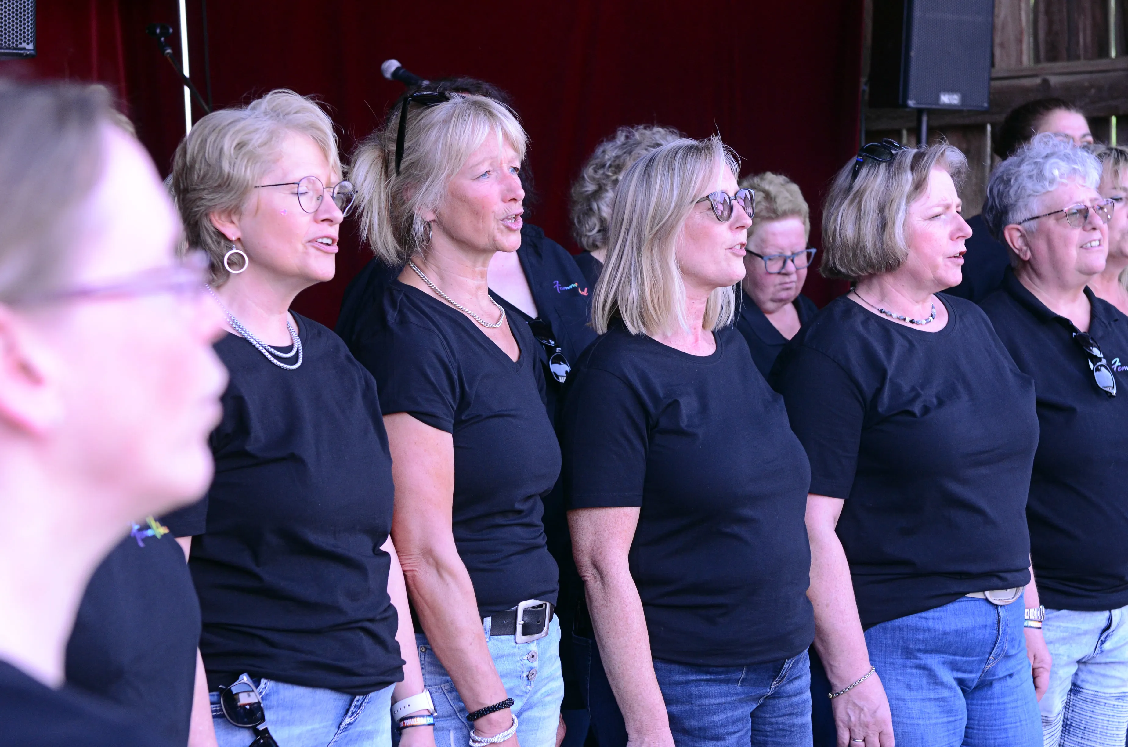 Chor aus Frauen singt auf der Bühne des I-Rock Festivals in Plettenberg. Die Sängerinnen tragen schwarze T-Shirts und Jeans.