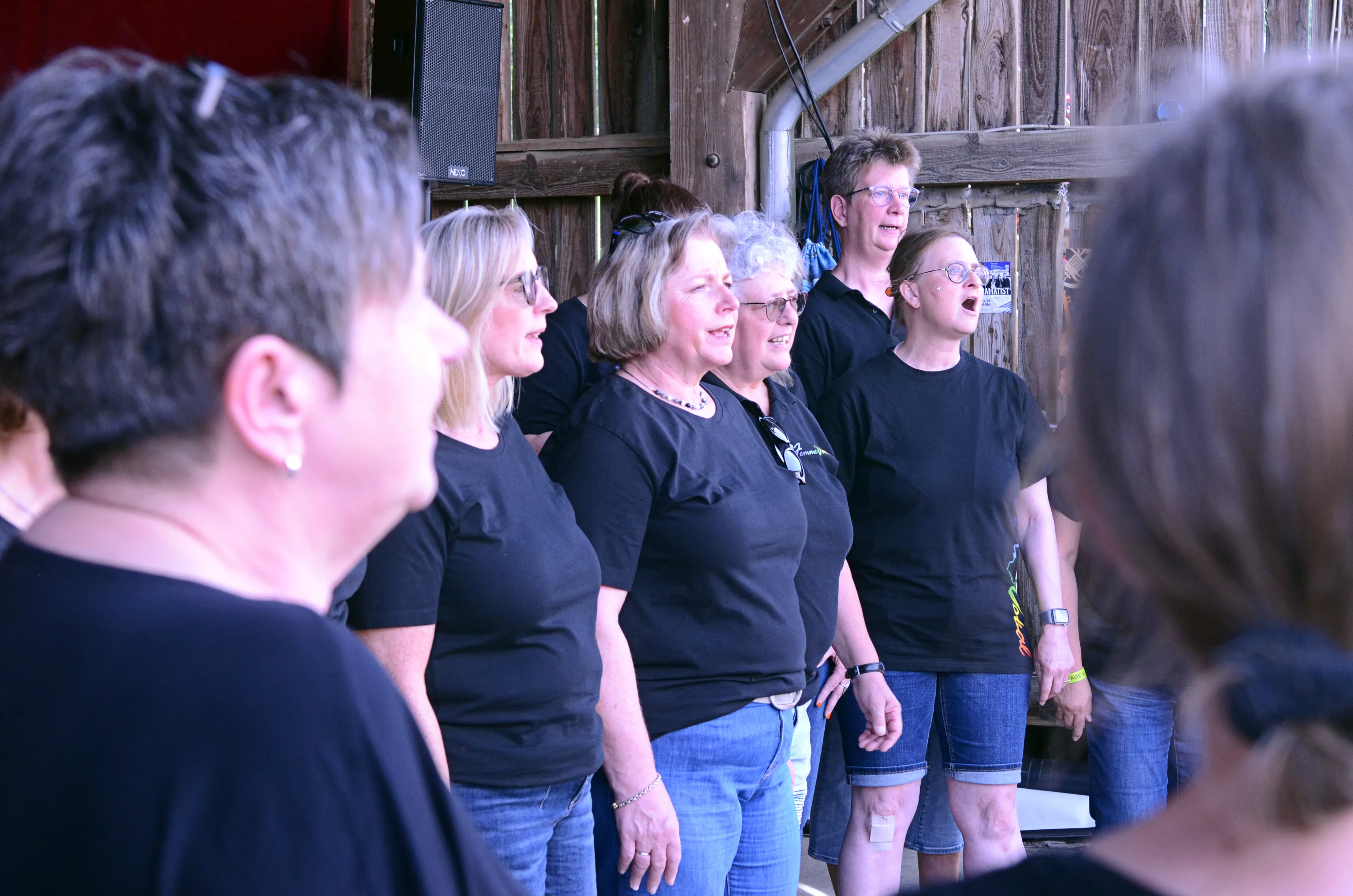 Frauenchor singt auf der Bühne des I-Rock Festivals in Plettenberg. Die Sängerinnen tragen schwarze T-Shirts und Jeans.