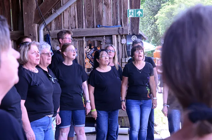 Chor singt auf der Bühne des I-Rock Festivals in Plettenberg. Die Gruppe besteht aus mehreren Frauen und Männern, die schwarze T-Shirts und Jeans tragen.