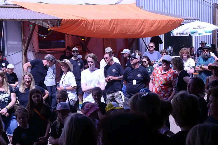 Menschenmenge vor einer Bühne mit orangefarbenem Sonnenschutz, im Hintergrund ein Stand mit dem Schriftzug 'Krombacher'.
