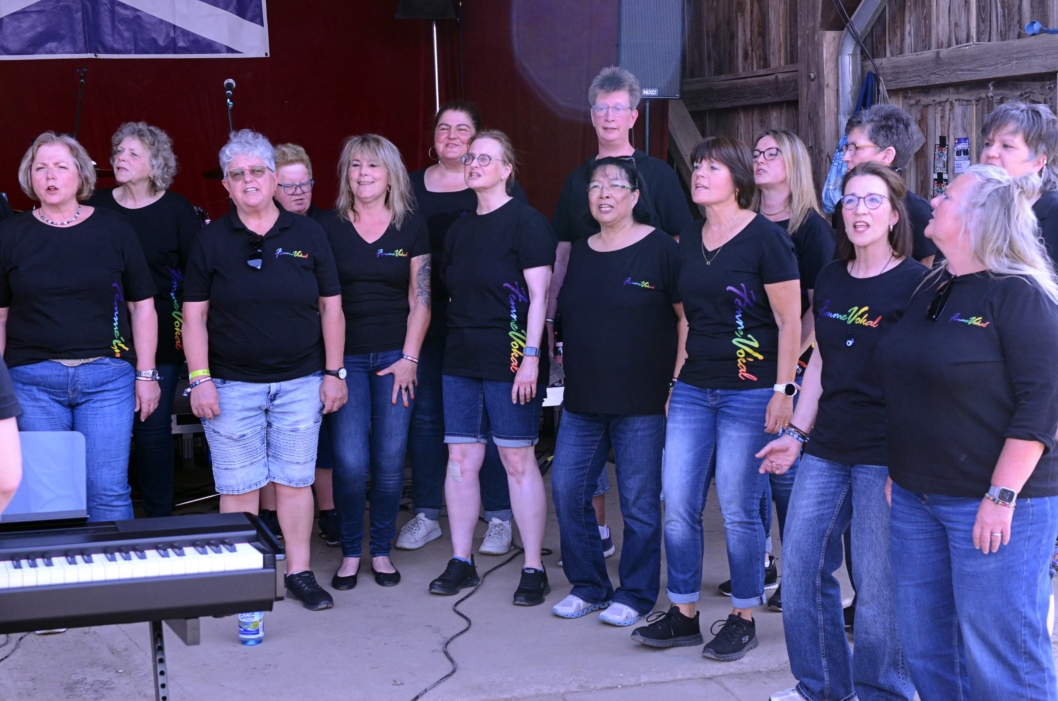 Chor „Femme Vocal“ singt auf der Bühne des I-Rock Festivals in Plettenberg. Die Gruppe besteht aus etwa 15 Frauen, die schwarze T-Shirts und Jeans tragen.