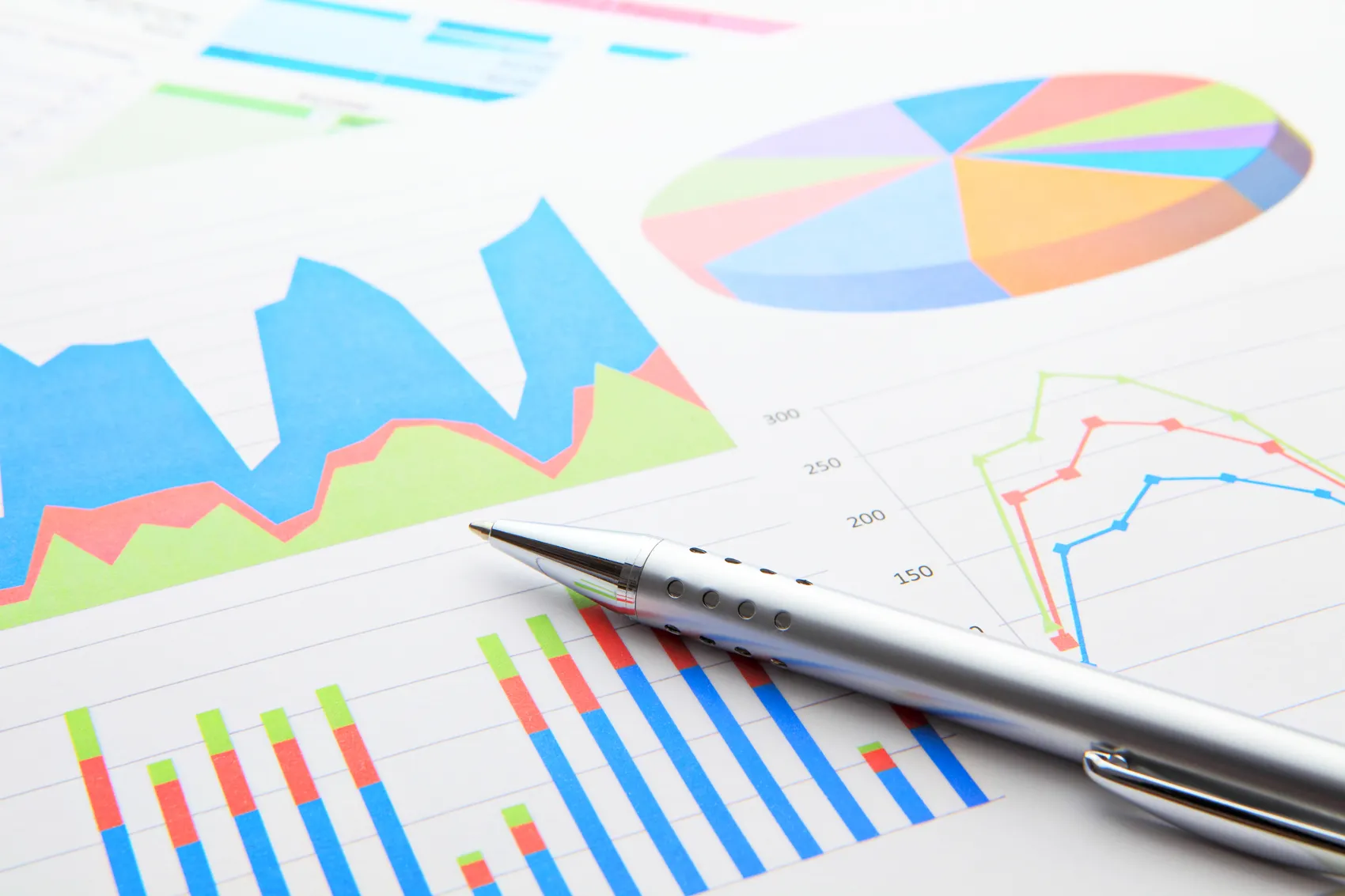 Diagramme und Grafiken mit steigenden und fallenden Werten, überlagert von einem silbernen Kugelschreiber.