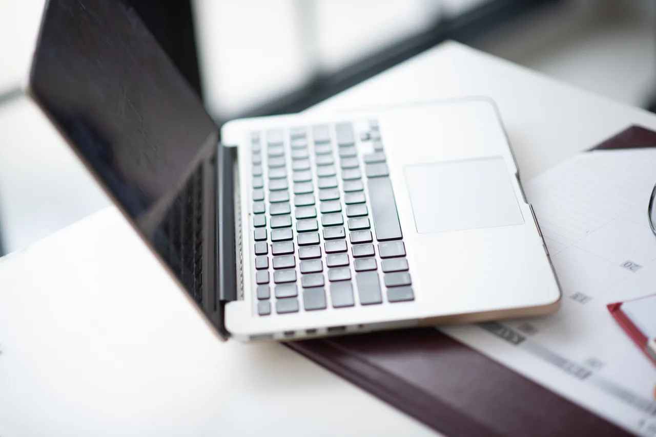 Geöffnetes Laptop auf einem Schreibtisch mit Papieren und einem Kalender.