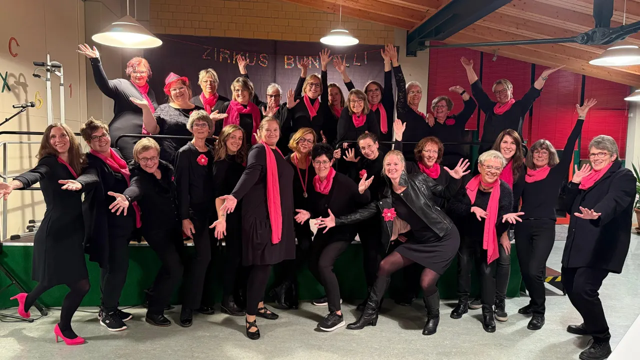 Große Gruppe von Frauen in Schwarz und Pink posiert lächelnd für ein Foto, viele mit hochgestreckten Armen. Im Hintergrund ein Banner mit der Aufschrift „Zirkus Bunttoll“.