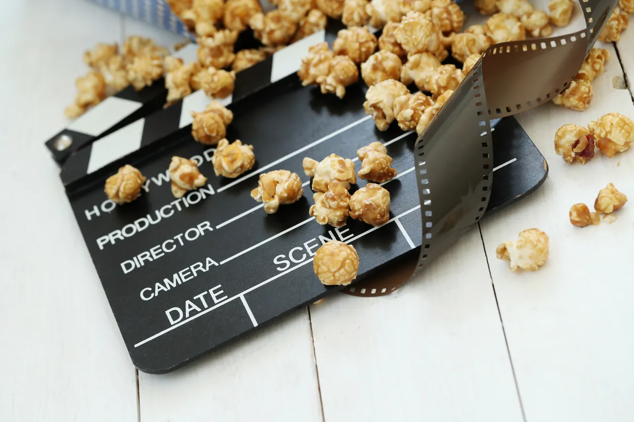 Ein Filmklappbrett und Popcorn auf einer weißen Holzoberfläche, die das Thema Film und Kino symbolisieren.