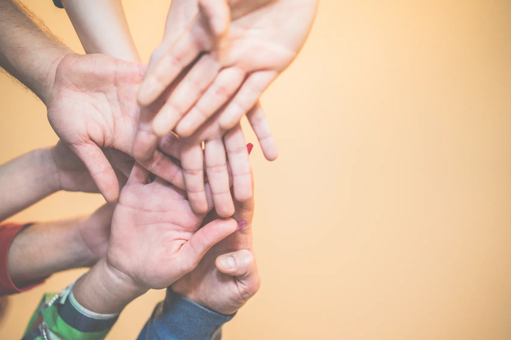 Mehrere Hände liegen übereinander, die Handflächen nach oben geöffnet. Das Bild symbolisiert Unterstützung, Zusammenarbeit und Gemeinschaft.