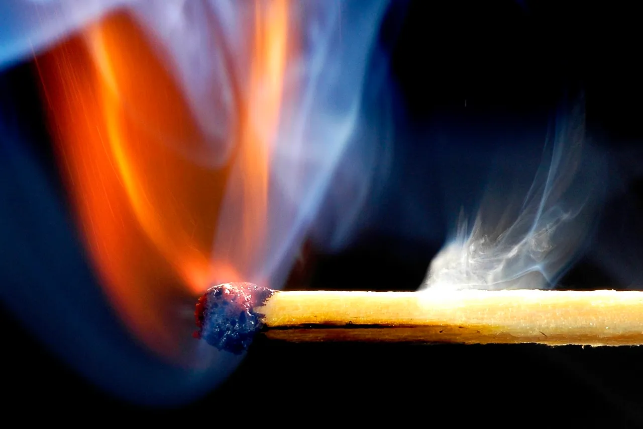 Brennender Streichholzende mit blauer Rauchwolke, Nahaufnahme. Symbol für Brandstiftung oder Zerstörung.