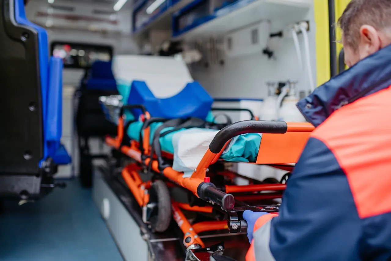 Ein leerer Rettungswagen mit einer orangefarbenen Trage und blauen Sitzen. Ein Sanitäter ist im Hintergrund zu sehen.