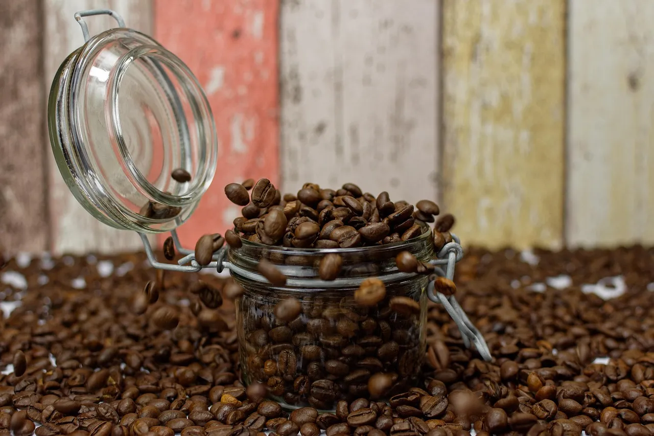 Ein offenes Glasgefäß voller Kaffeebohnen vor einem Hintergrund aus bunten Holzbrettern.