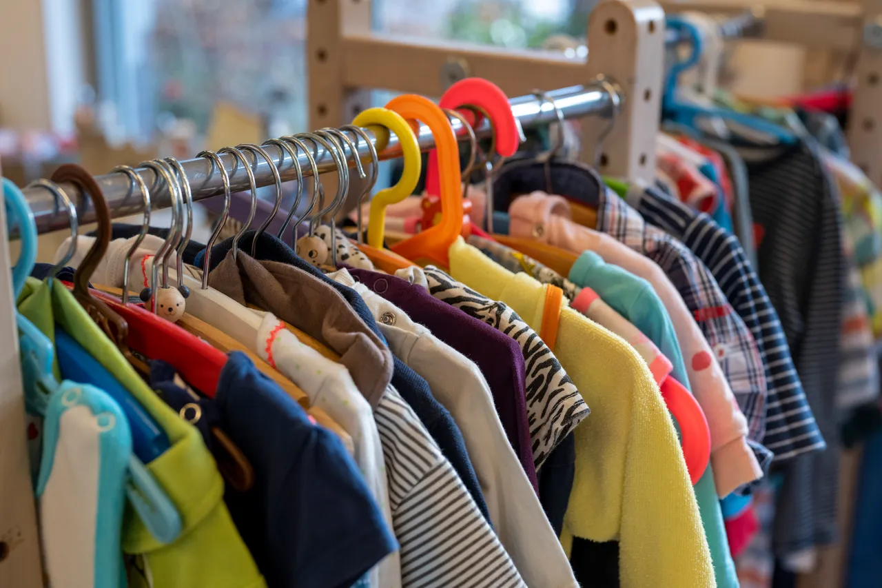 Bunte Kinderkleidung hängt auf einem Kleiderbügel an einer Stange, wie sie auf einem Flohmarkt oder Basar zu finden ist.
