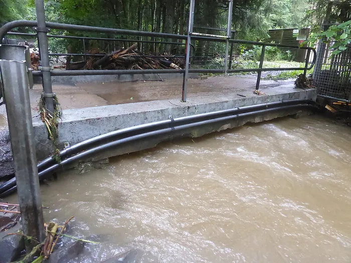 Trübes Hochwasser fließt unter einer Betonbrücke mit Metallgeländer.