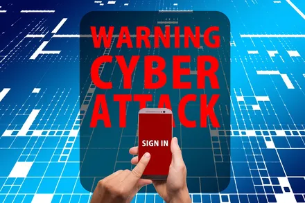 Eine Hand hält ein Smartphone mit dem Aufruf „Sign in“ vor einem Hintergrund aus binärem Code und dem Warnhinweis „Cyber Attack“.