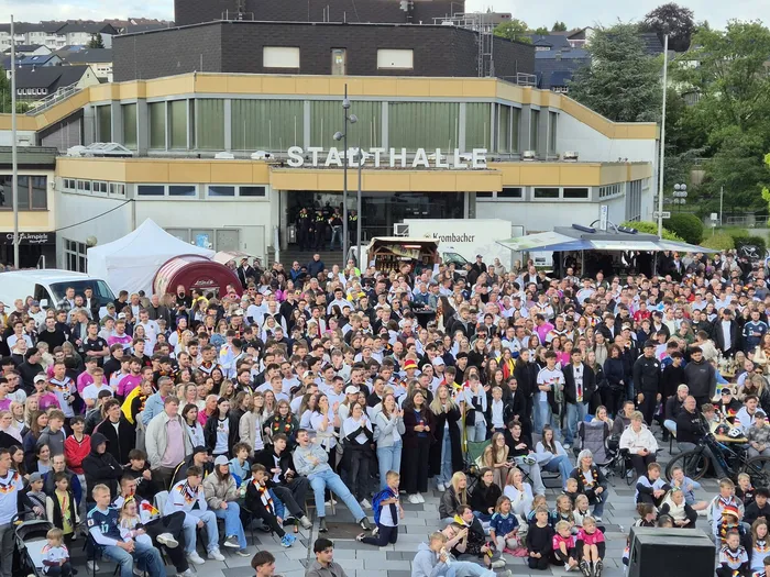 Große Menschenmenge jubelt vor einem Gebäude mit dem Schriftzug „Stadthalle“. Viele Zuschauer halten Deutschlandflaggen hoch.