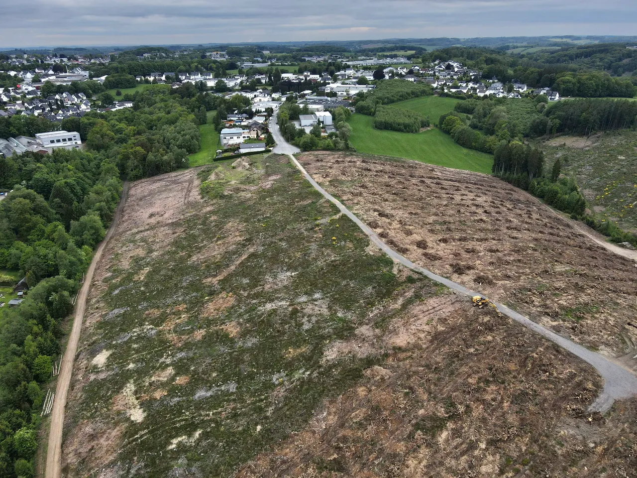 Gerodete Fläche für das geplante Industriegebiet Leifersberge, im Hintergrund eine Wohnsiedlung und bewaldete Hügel.