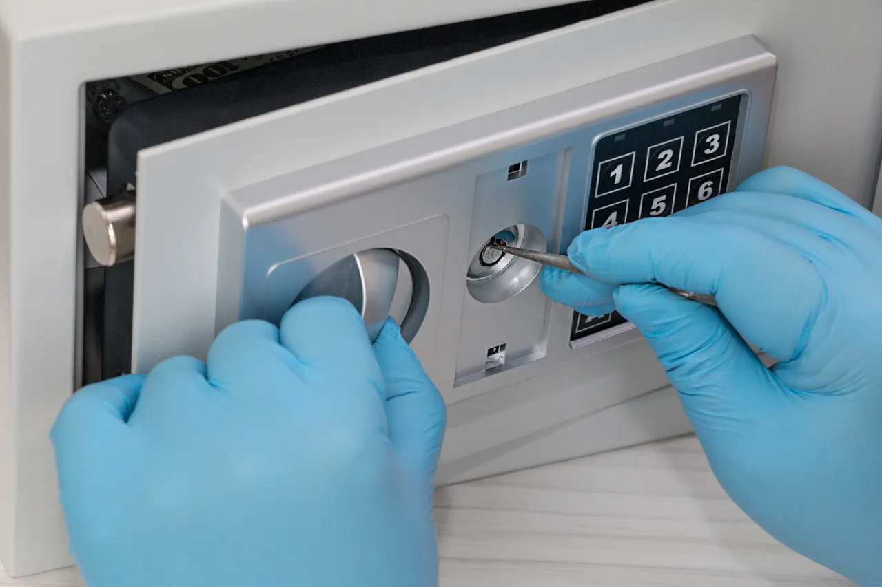 Blaue Handschuhe öffnen ein Zahlenschloss an einem Tresor mit einem Werkzeug.