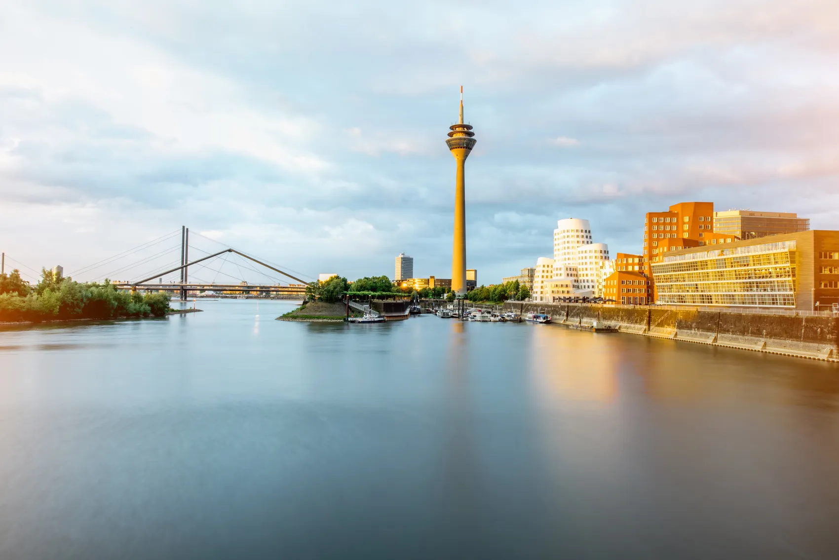 Blick über den Rhein auf die Skyline Düsseldorfs mit dem Rheinturm, der Kennedybrücke und modernen Gebäuden am Ufer.