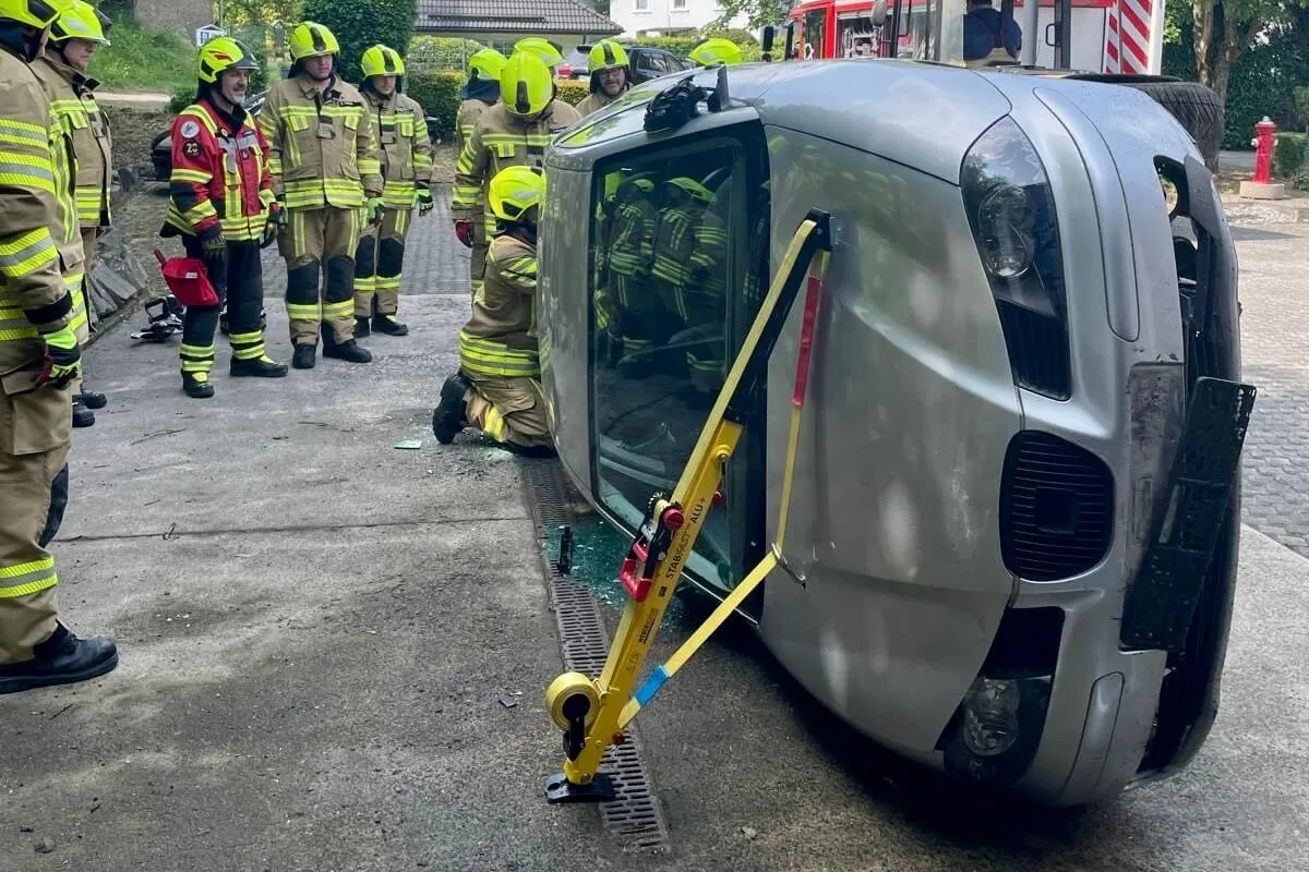 Umgestürztes Auto wird von Feuerwehrleuten mit speziellem Hebesystem stabilisiert, während weitere Einsatzkräfte beobachten.