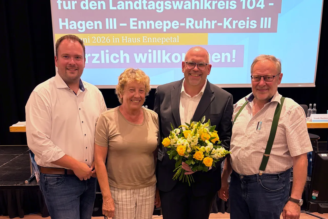 Vier Personen stehen auf einer Bühne vor einem Banner mit der Aufschrift “für den Landtagswahlkreis 104 - Hagen III - Ennepe-Ruhr-Kreis III”. Der Mann in der Mitte hält einen Blumenstrauß. Es sind der Vorsitzende Alexander Ebbert, die stellvertretende Vorsitzende Ulrike Borowski, Veit Kuhl und der stellvertretende Vorsitzende Martin Gensler.