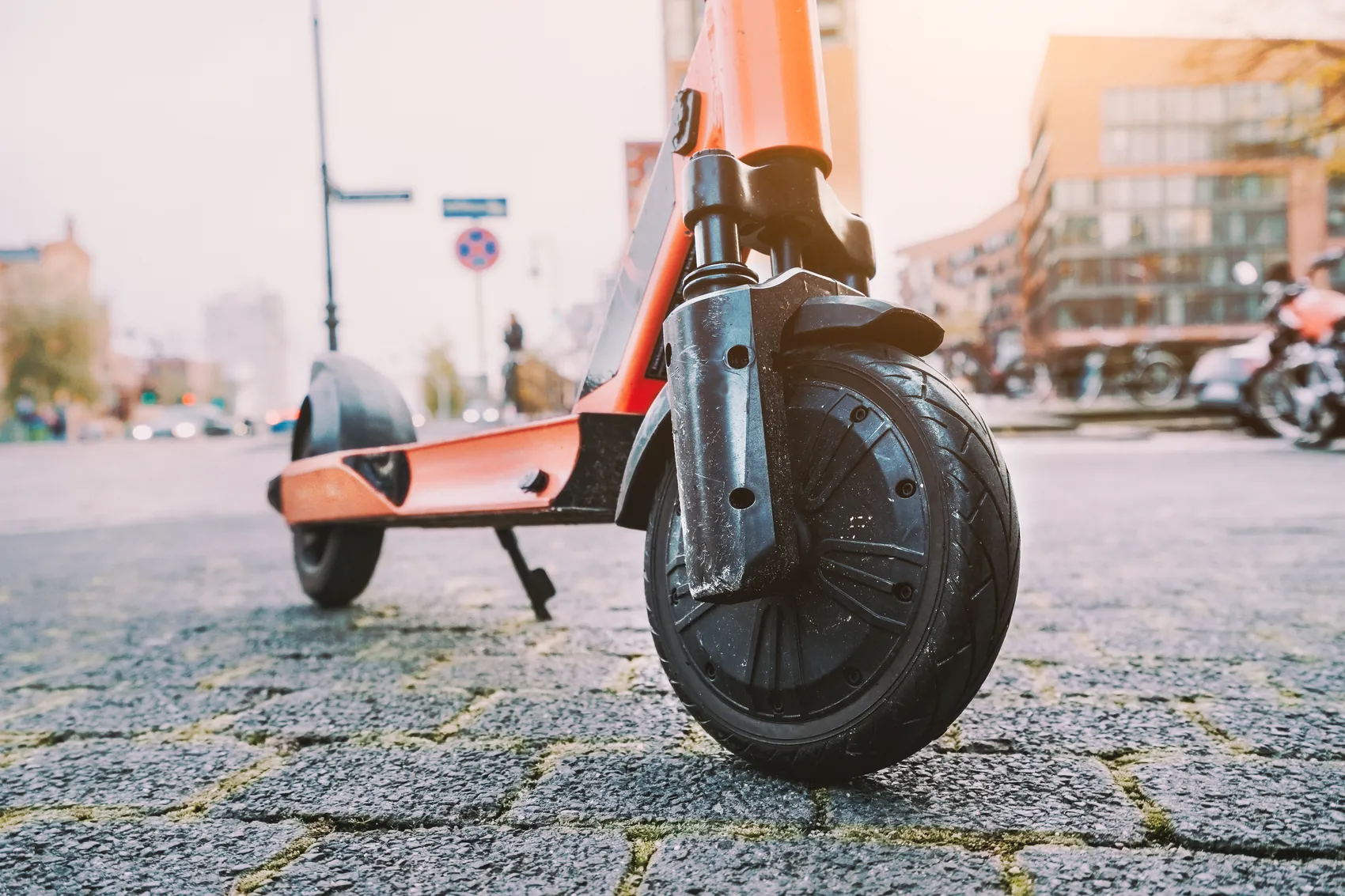 Nahaufnahme eines orangefarbenen E-Scooters auf Kopfsteinpflaster in einer städtischen Umgebung.